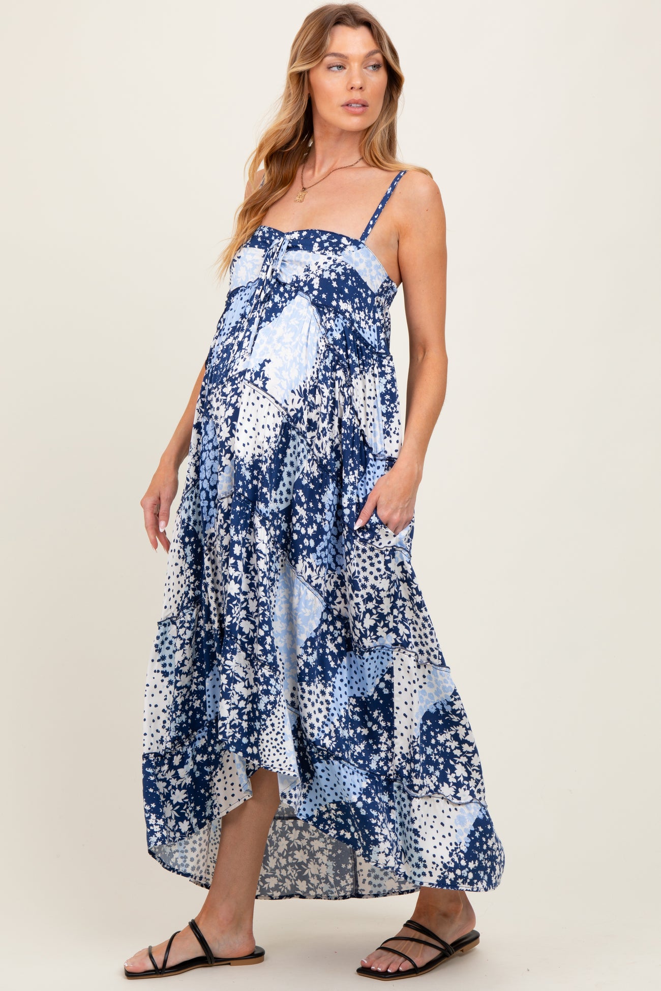 woman wearing a navy and white floral print maternity maxi dress with pockets and adjustable straps, showing her baby bump