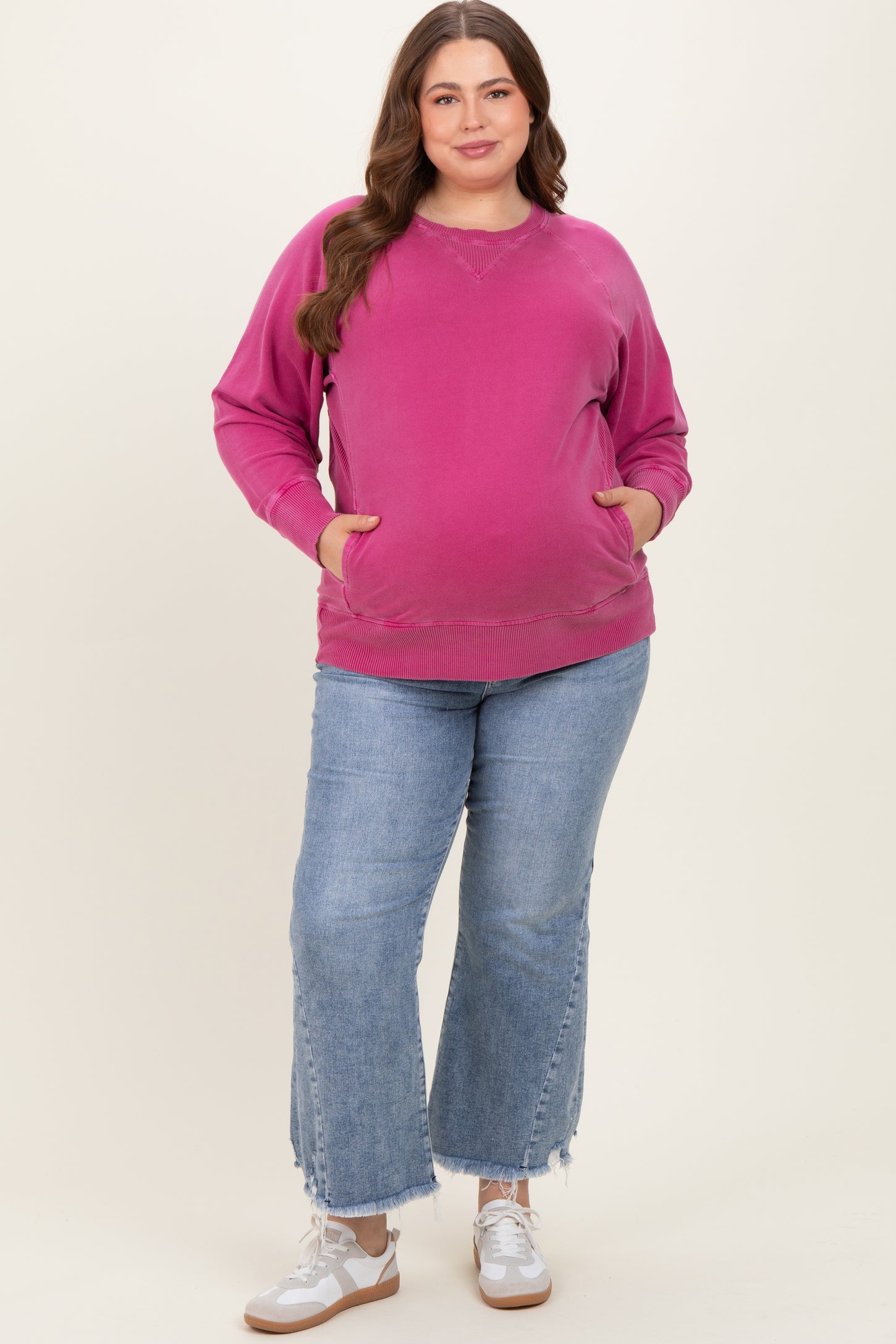 woman wearing a hot pink maternity sweatshirt with pockets, paired with light blue flared jeans and white sneakers