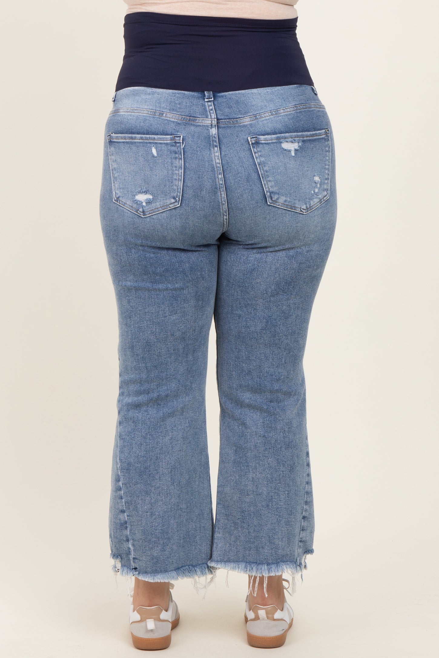 woman wearing light blue distressed maternity plus flared jeans with a navy waistband, showing her baby bump from the back