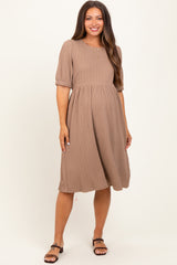 woman wearing a taupe maternity dress with puff sleeves and a tiered skirt, showing her baby bump