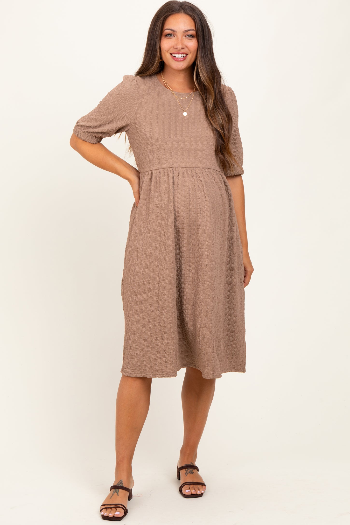 woman wearing a taupe maternity dress with short puff sleeves and a fitted bodice, showing her baby bump