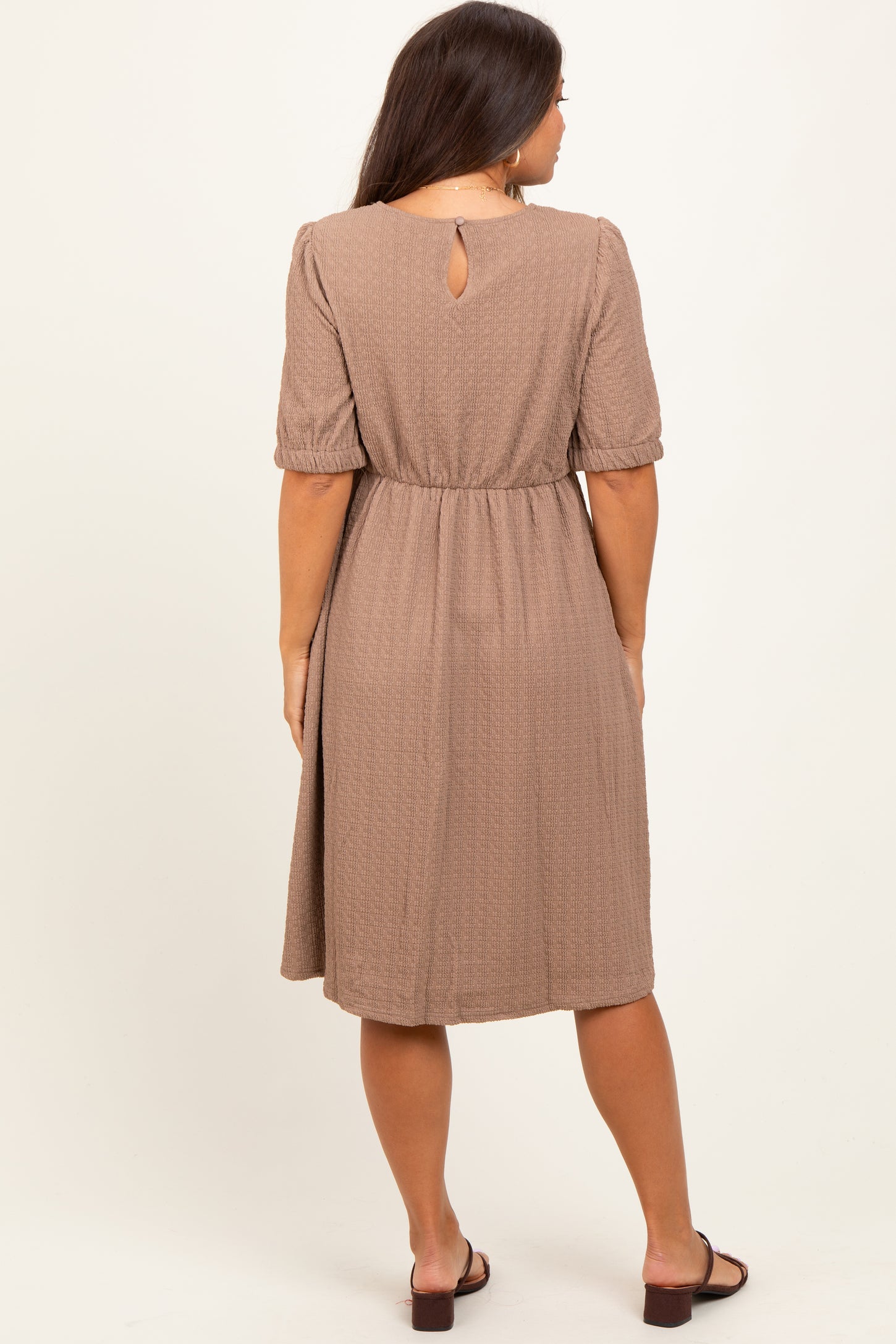 woman wearing a brown maternity dress with a keyhole back and puff sleeves, showcasing a relaxed silhouette
