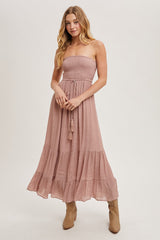 woman wearing a dusty pink strapless maxi dress with a smocked bodice and tiered hem, paired with tan ankle boots
