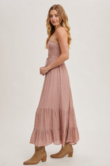 woman wearing a dusty rose strapless maxi dress with a smocked bodice and tiered ruffle hem, styled with tan ankle boots