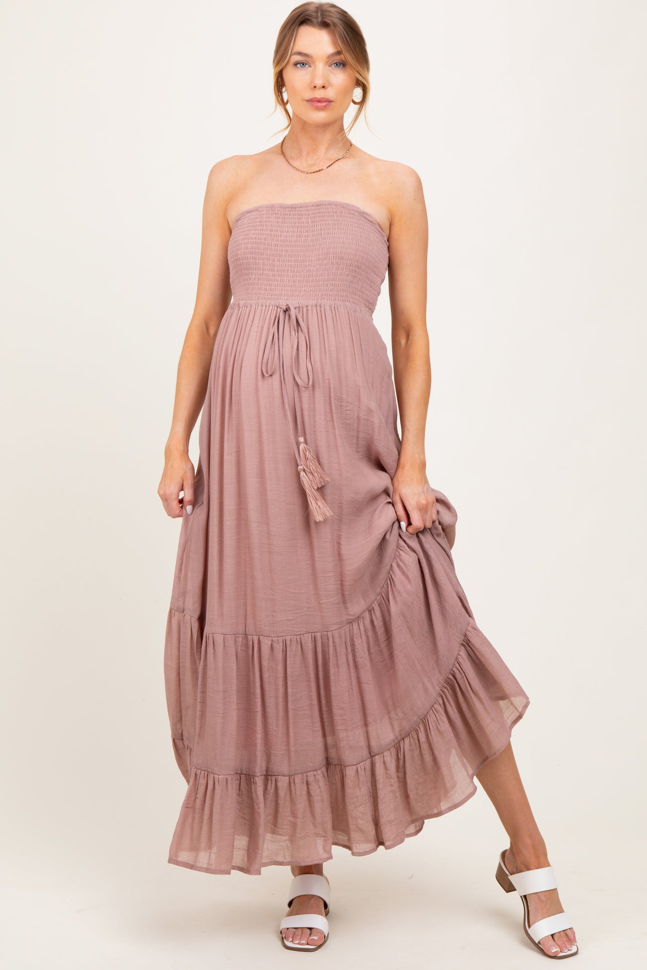woman wearing a strapless mauve maternity maxi dress with a smocked bodice and tiered ruffle hem, showing her baby bump