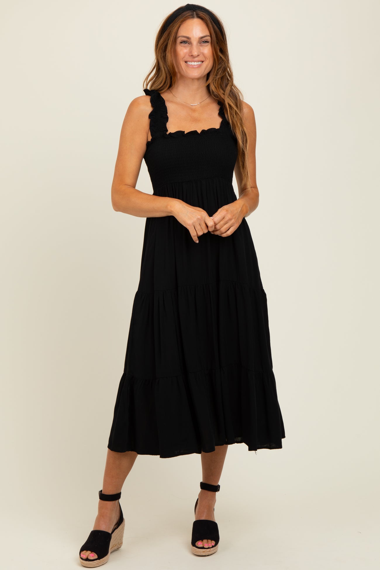 woman wearing a black tiered midi dress with ruffle straps and a fitted bodice, styled with wedge sandals