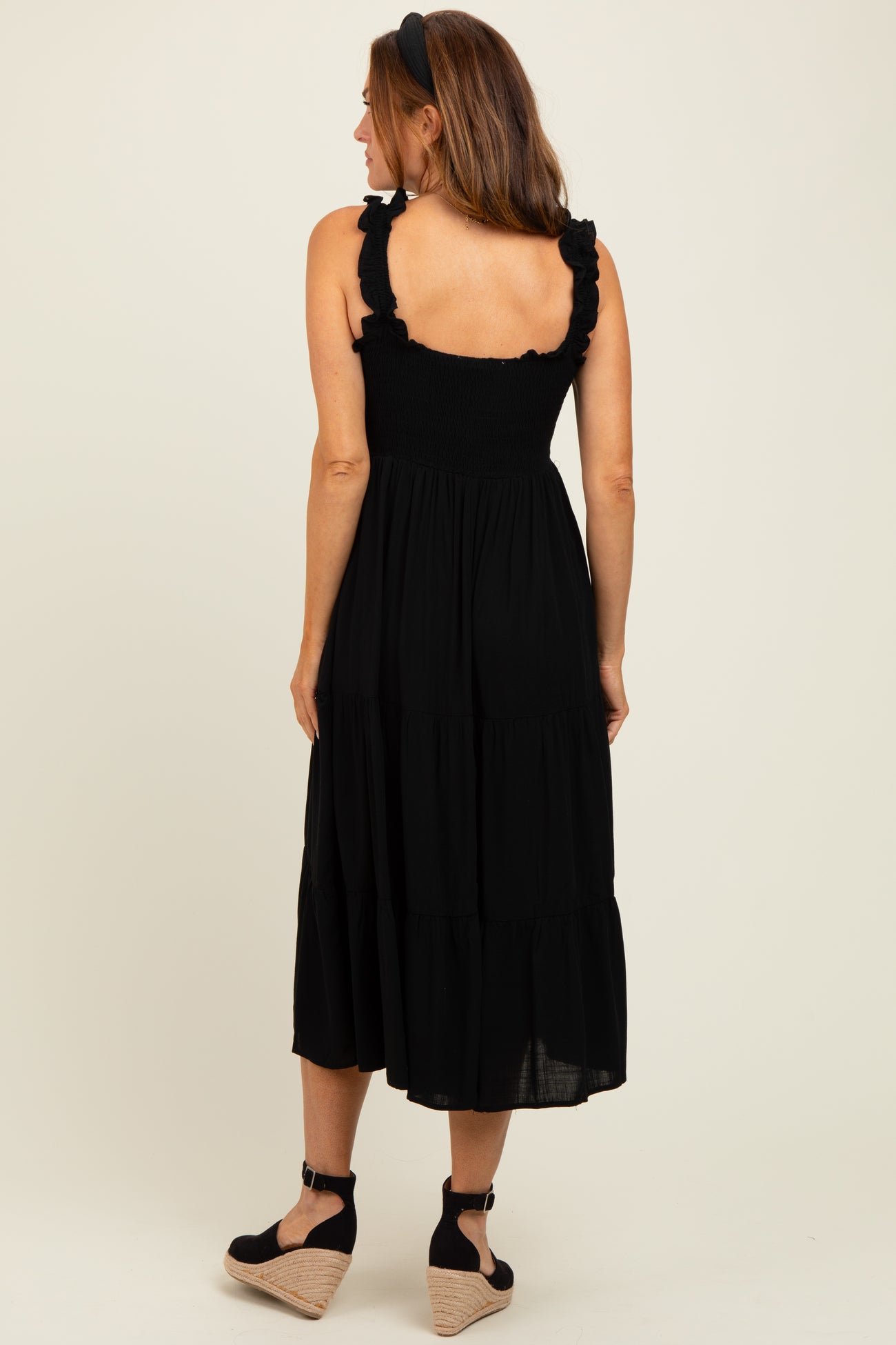 woman wearing a black tiered midi dress with ruffled straps and a fitted bodice, seen from the back