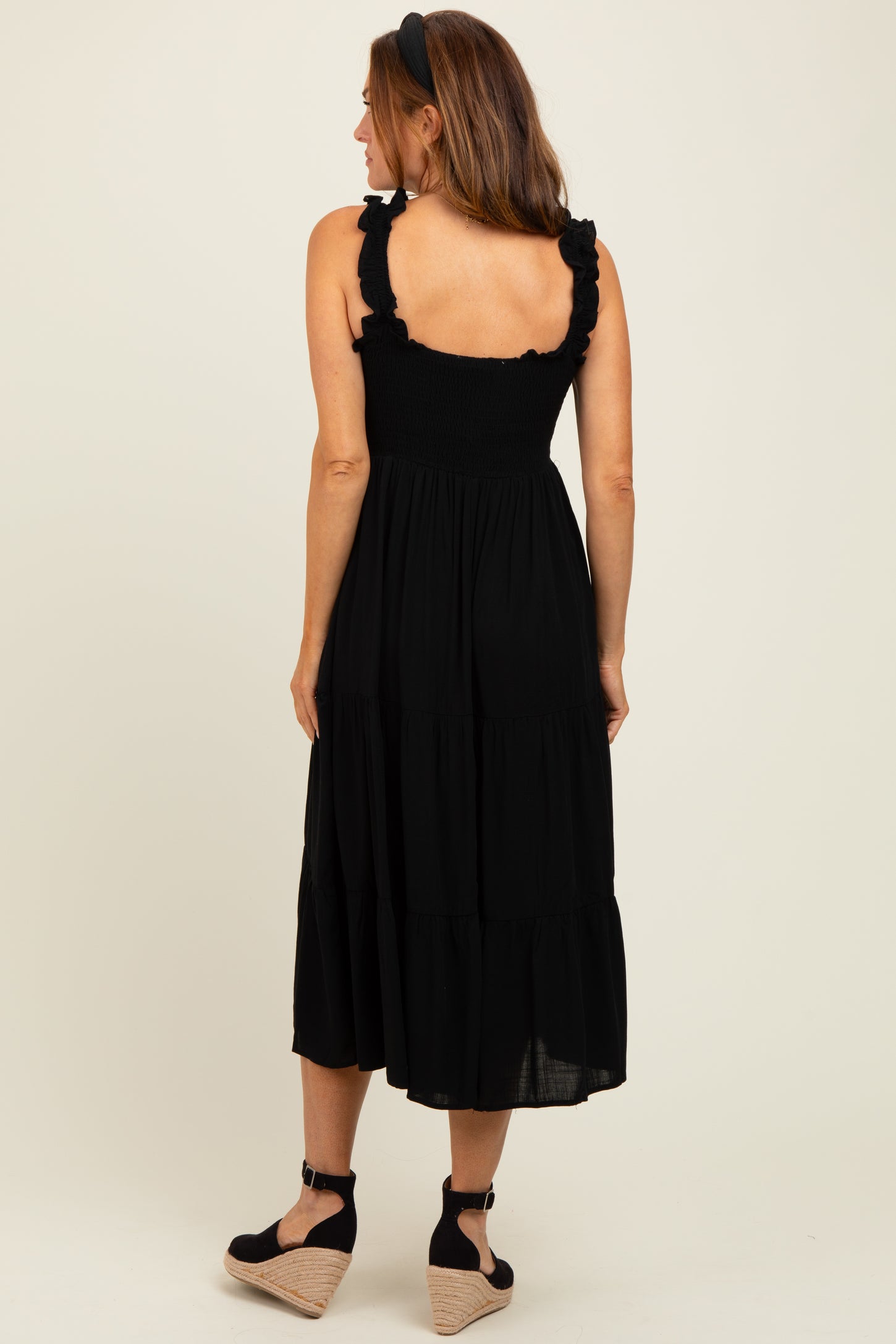 woman wearing a black tiered midi dress with ruffled straps and a fitted bodice, seen from the back