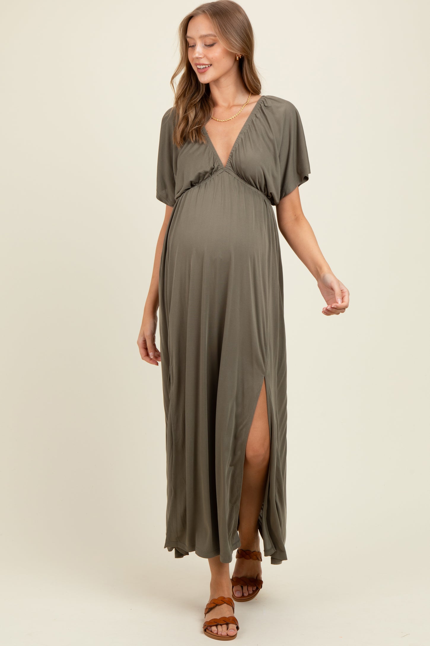 woman wearing an olive green short sleeve maternity maxi dress with a deep v-neck and a side slit, showing her baby bump