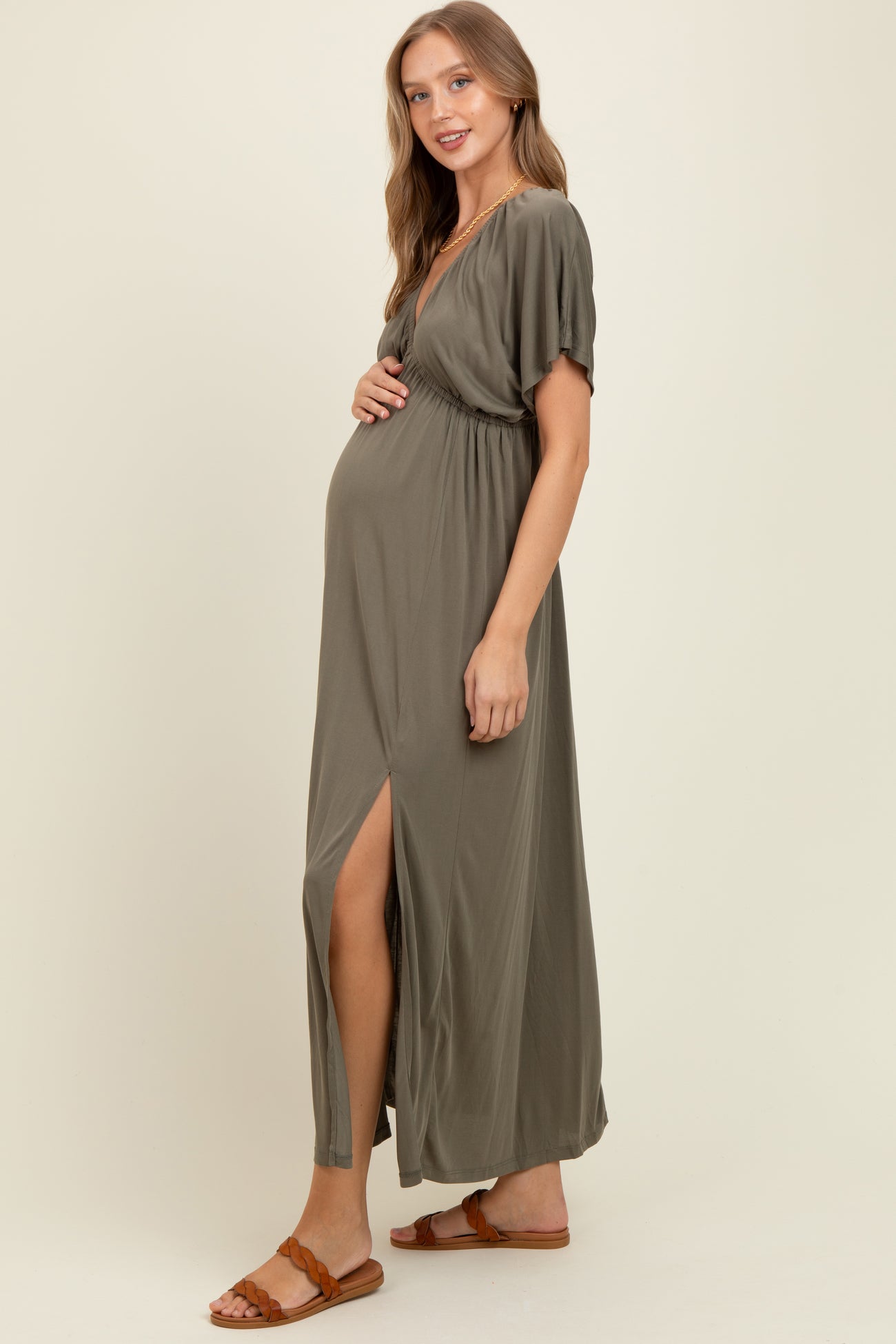 woman wearing a dark olive green maternity maxi dress with a slit, highlighting her baby bump