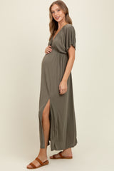 woman wearing a dark olive green maternity maxi dress with a slit, highlighting her baby bump