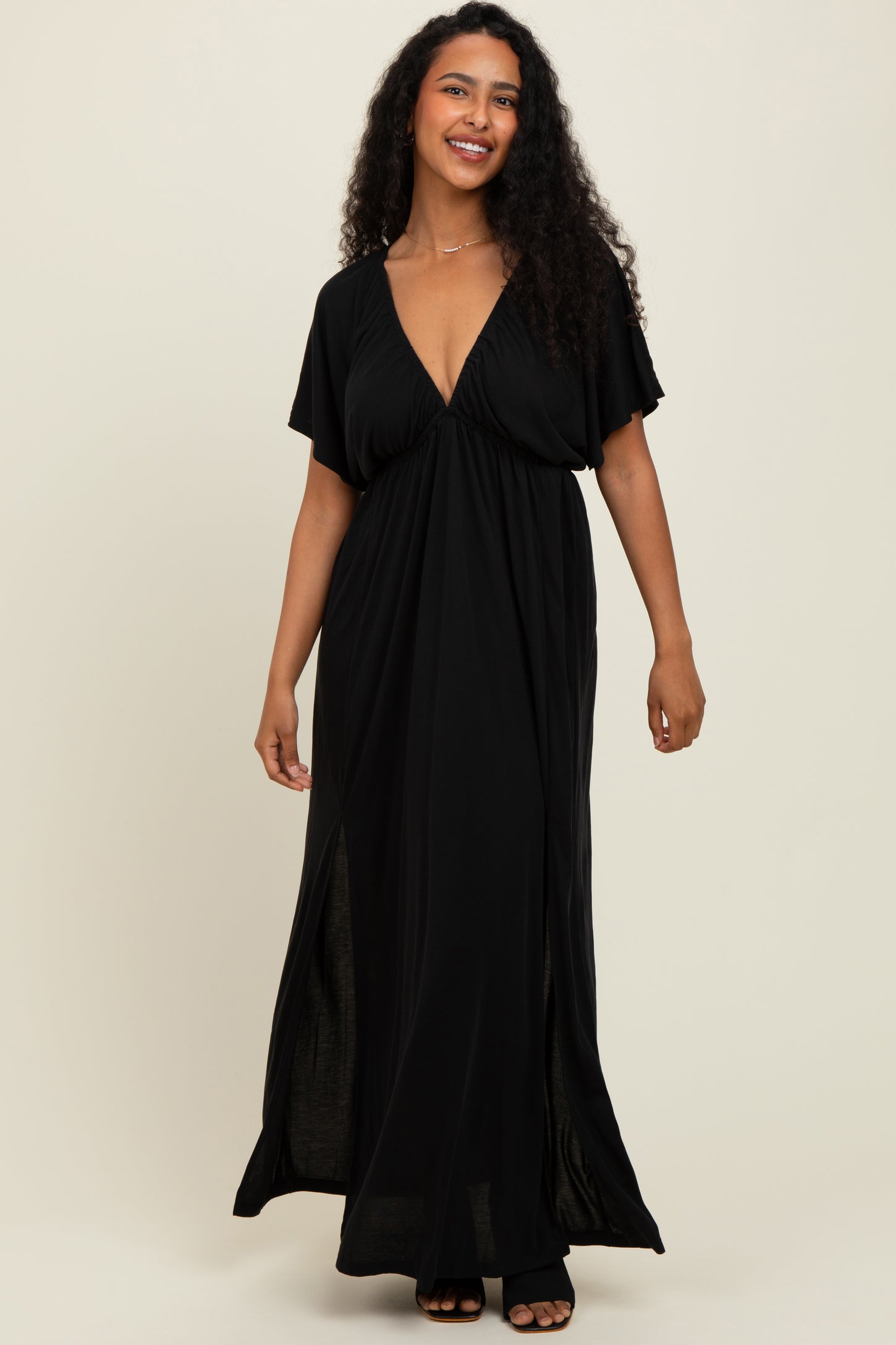 woman wearing a black maxi dress with a deep v-neck and short sleeves, standing and smiling