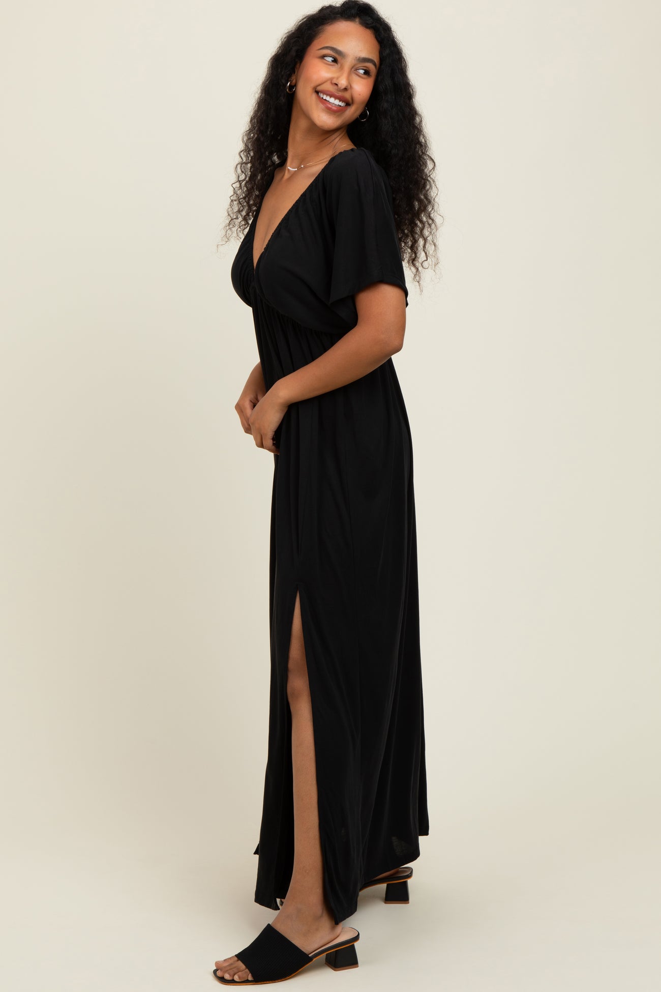 woman wearing a black maxi dress with a deep v-neck and side slit, standing sideways with a smile