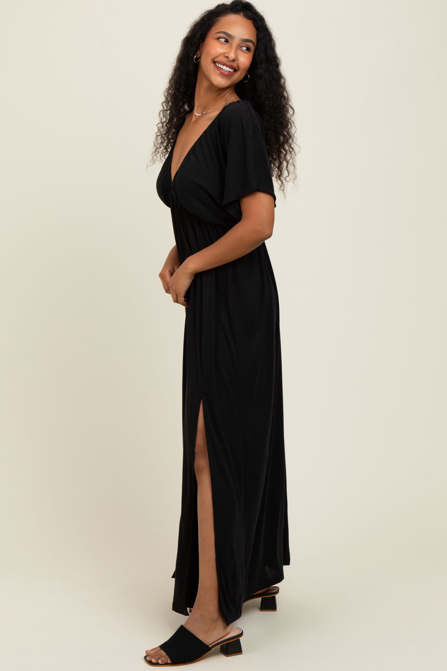 woman wearing a black maxi dress with a deep v-neck and side slit, standing sideways with a smile