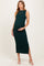 woman wearing a dark green ribbed maternity dress, holding her baby bump, paired with strappy white sandals