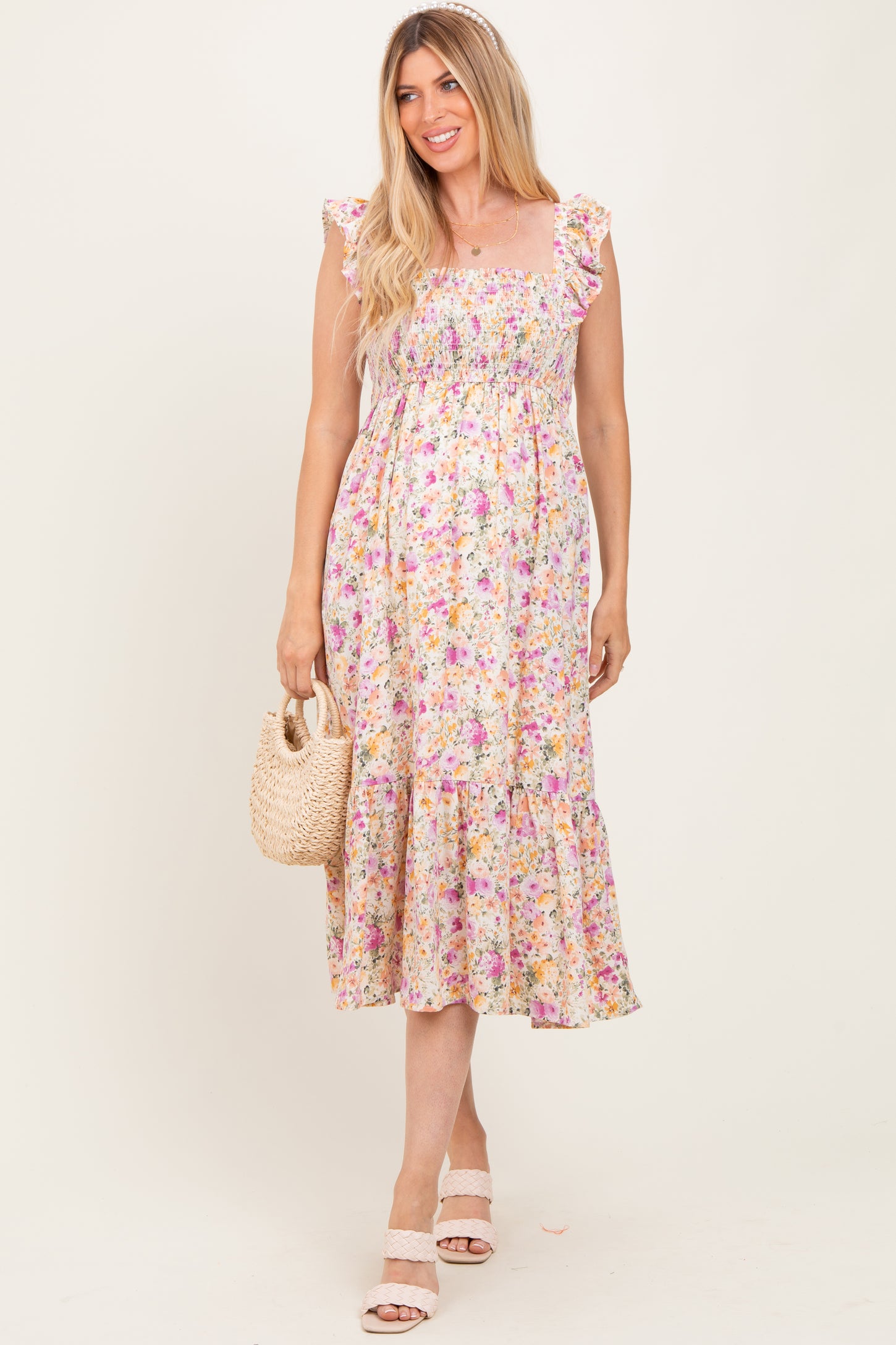 woman wearing a floral maternity maxi dress with ruffled straps and a tiered skirt, holding a woven bag