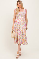 woman wearing a floral maternity maxi dress with ruffled straps and a tiered skirt, holding a woven bag