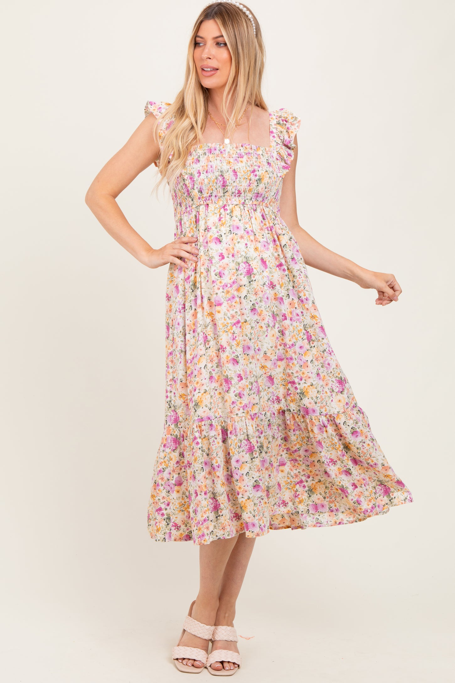 woman wearing a floral print maternity dress with ruffle sleeves and a flowy skirt, standing with one hand on her hip