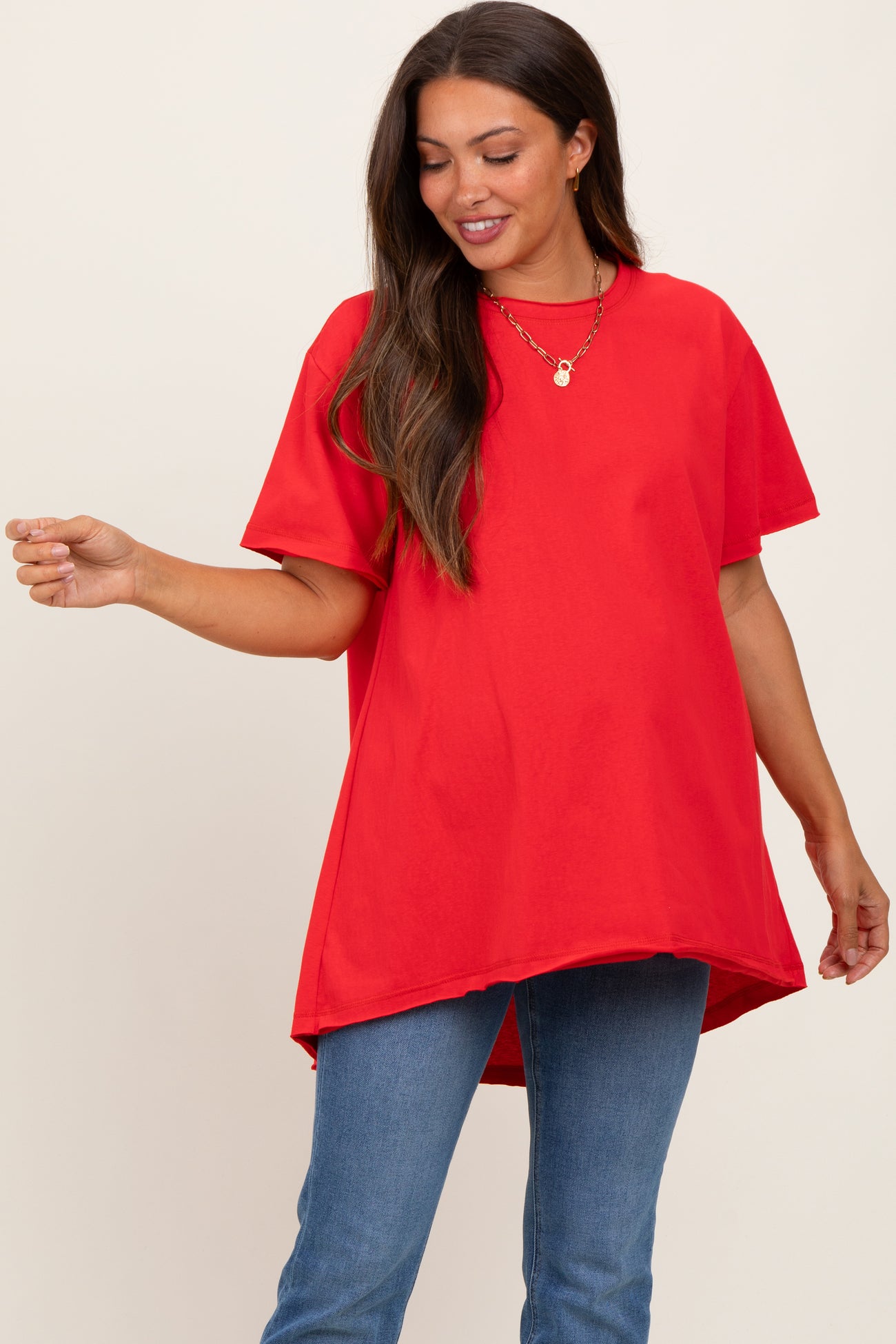 woman wearing a red oversized maternity t-shirt with a rounded hem and a visible baby bump, paired with blue jeans
