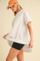 woman wearing a white oversized t-shirt and black biker shorts, holding the shirt slightly up, stylish baseball cap on her head