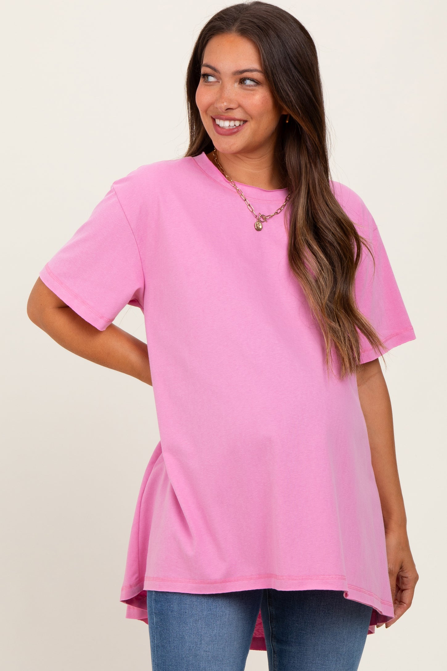 woman wearing a pink short sleeve maternity top with a longer hem and smiling