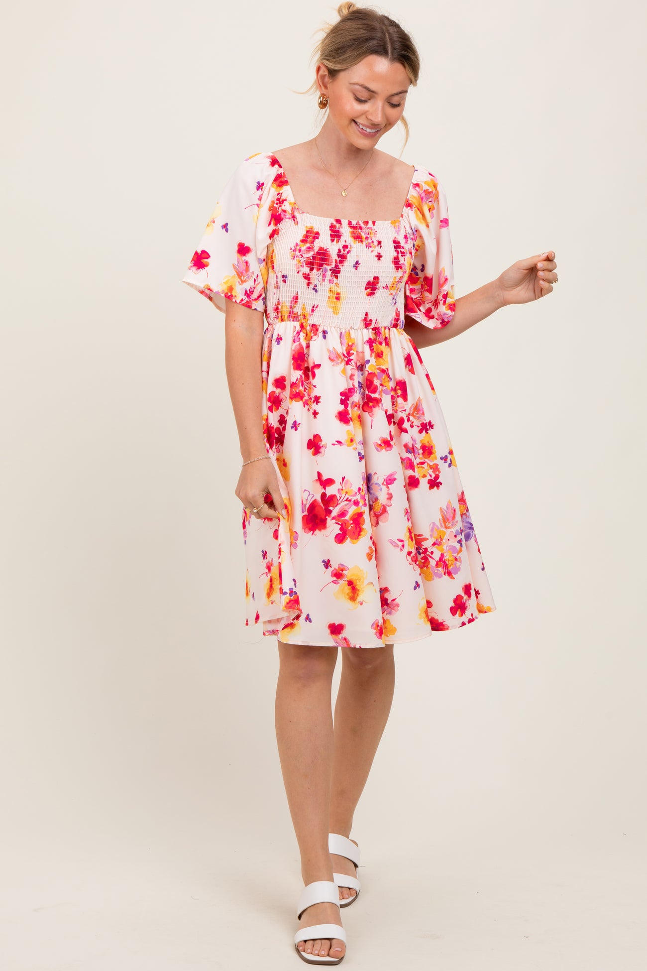 woman wearing a pink floral smocked dress with puff sleeves and a square neckline, smiling and standing in a light pose