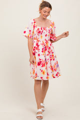woman wearing a pink floral smocked dress with puff sleeves and a square neckline, smiling and standing in a light pose