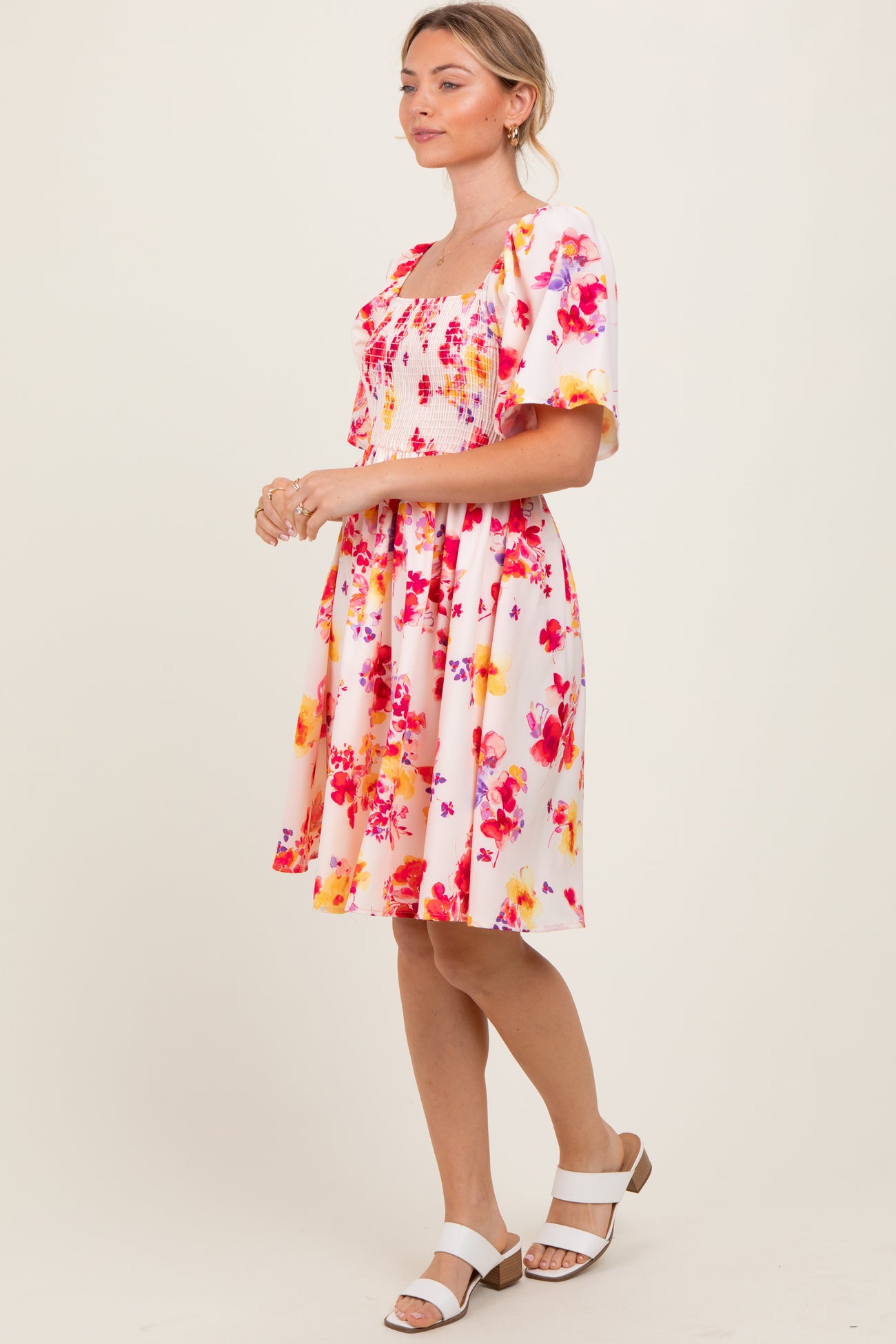 woman wearing a pink floral short sleeve dress with a square neckline and smocked bodice, standing in profile