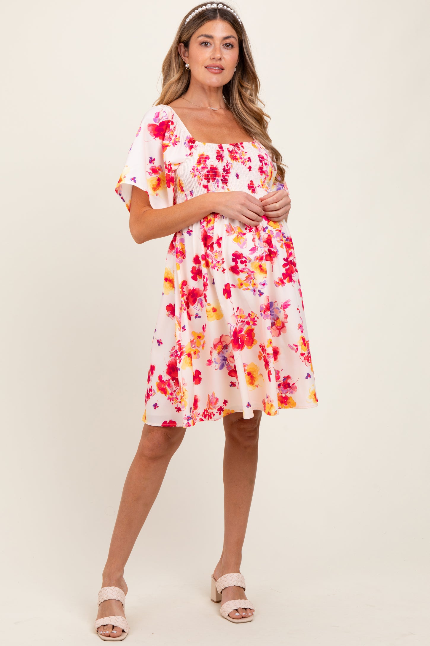 woman wearing a floral print short sleeve maternity dress with a square neckline and pink and orange hues, holding her baby bump