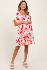 woman wearing a floral print short sleeve maternity dress with a square neckline and pink and orange hues, holding her baby bump