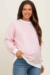 woman wearing a light pink striped maternity sweatshirt with white cuffs, showing her baby bump