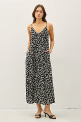 woman wearing a black floral maxi dress with adjustable straps and pockets, styled with black heeled sandals