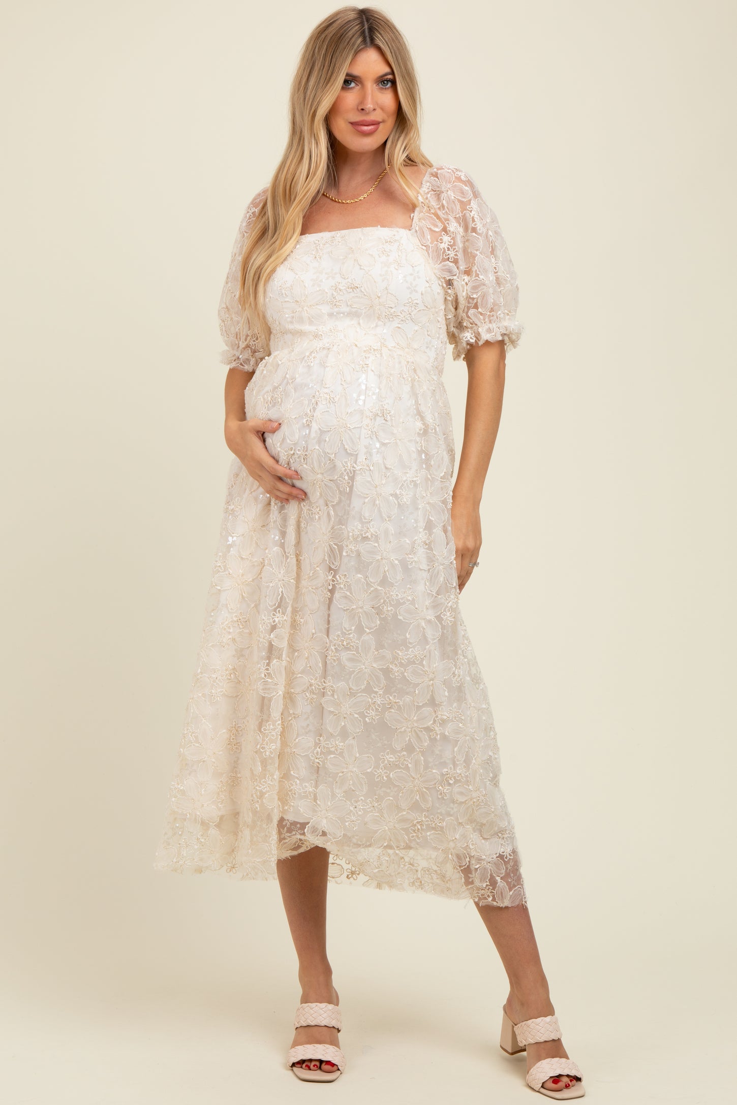 woman wearing a cream floral lace maternity dress and showing her baby bump