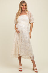 woman wearing a cream floral lace maternity dress and showing her baby bump