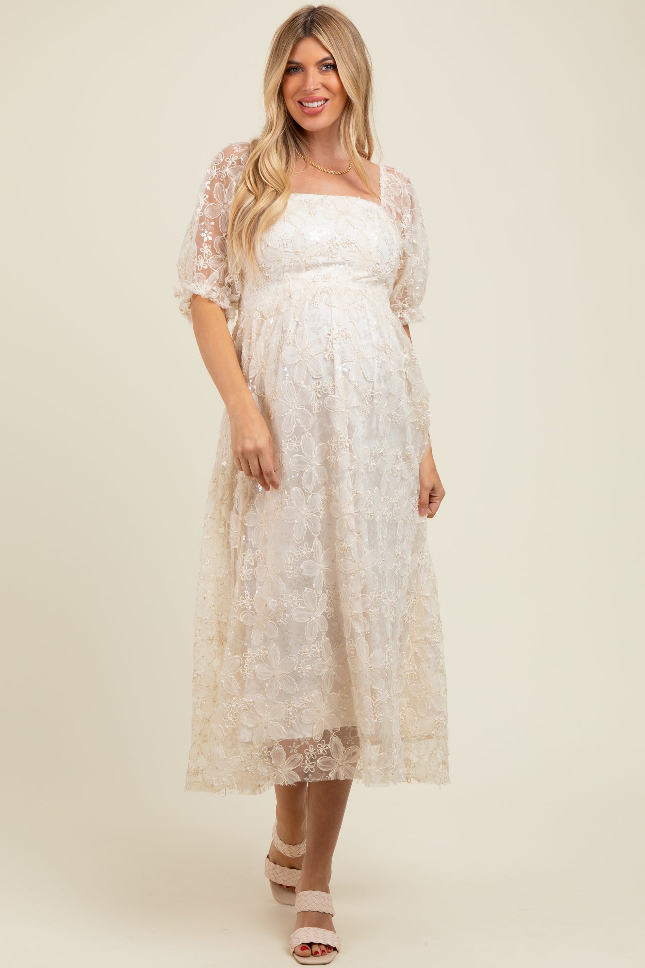 woman wearing a cream lace maternity dress with a square neckline and puff sleeves, showing off her baby bump