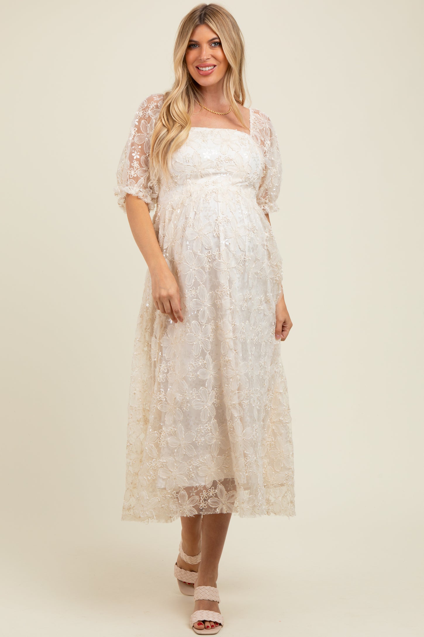 woman wearing a cream lace maternity dress with a square neckline and puff sleeves, showing off her baby bump