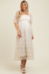 woman wearing a cream lace maternity dress with a square neckline and puff sleeves, showing off her baby bump