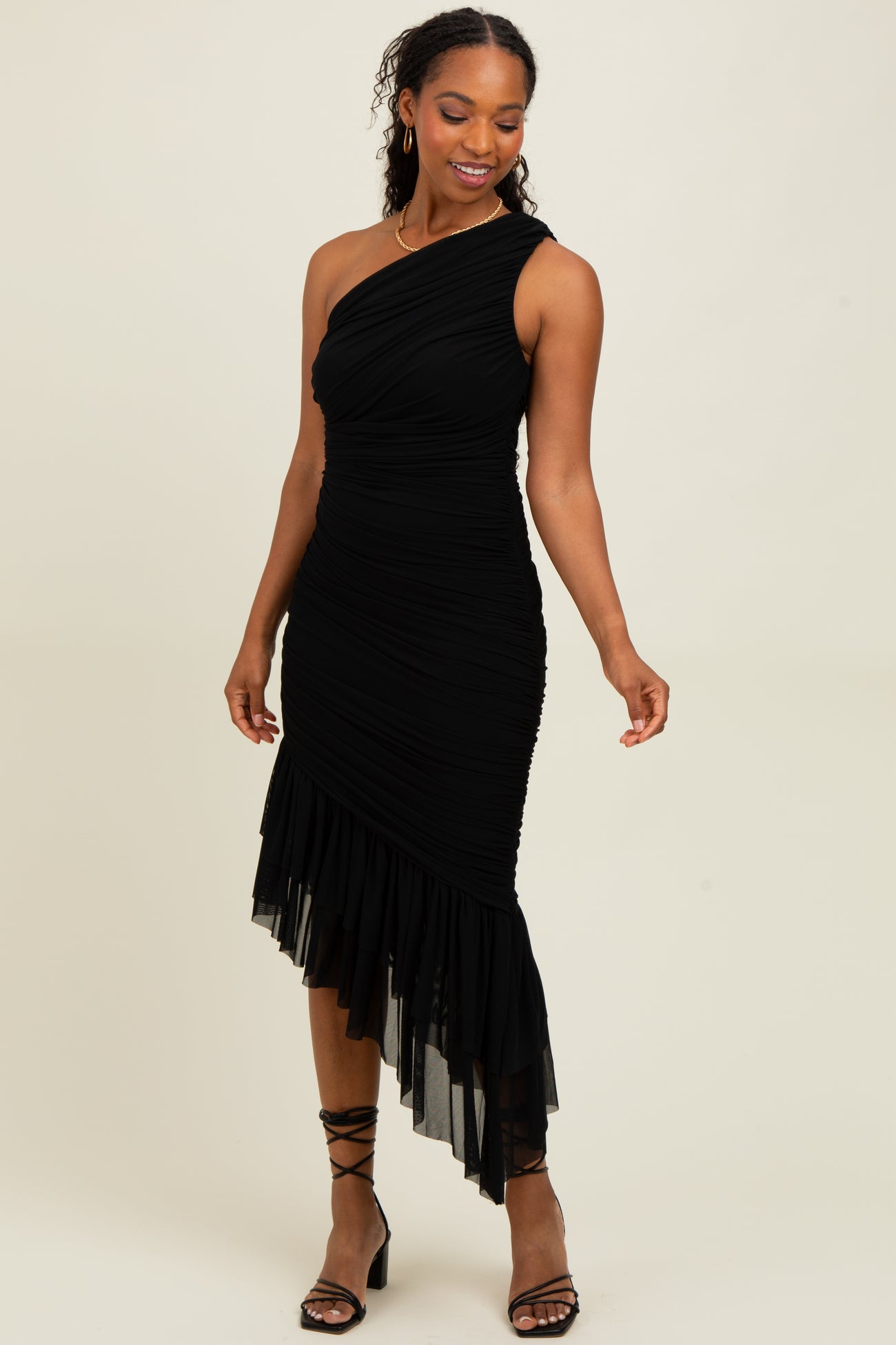 woman wearing a black one-shoulder ruched dress with a handkerchief hemline and strappy heels