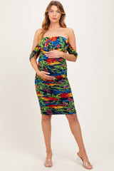 woman wearing a colorful floral off-shoulder maternity dress and holding her baby bump