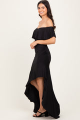 woman wearing a black off-the-shoulder dress with ruffle details and a high-low hemline, posing sideways