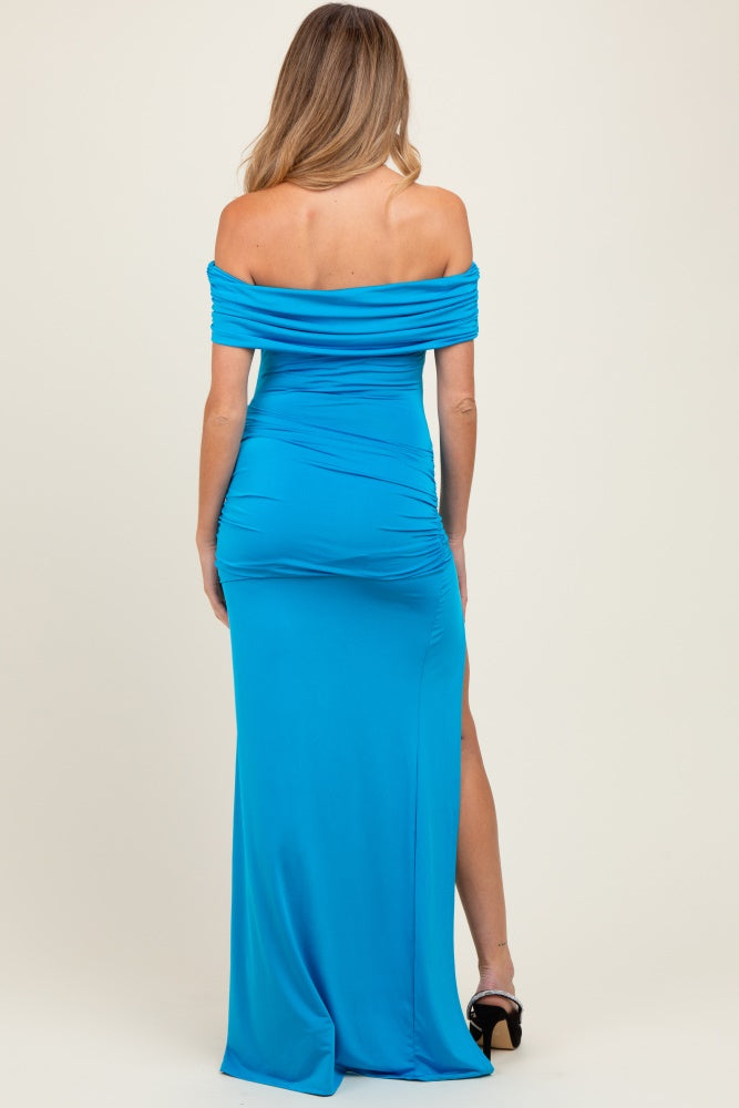 woman wearing a bright blue off-the-shoulder maternity gown with ruching and a side slit, showing her pregnancy belly