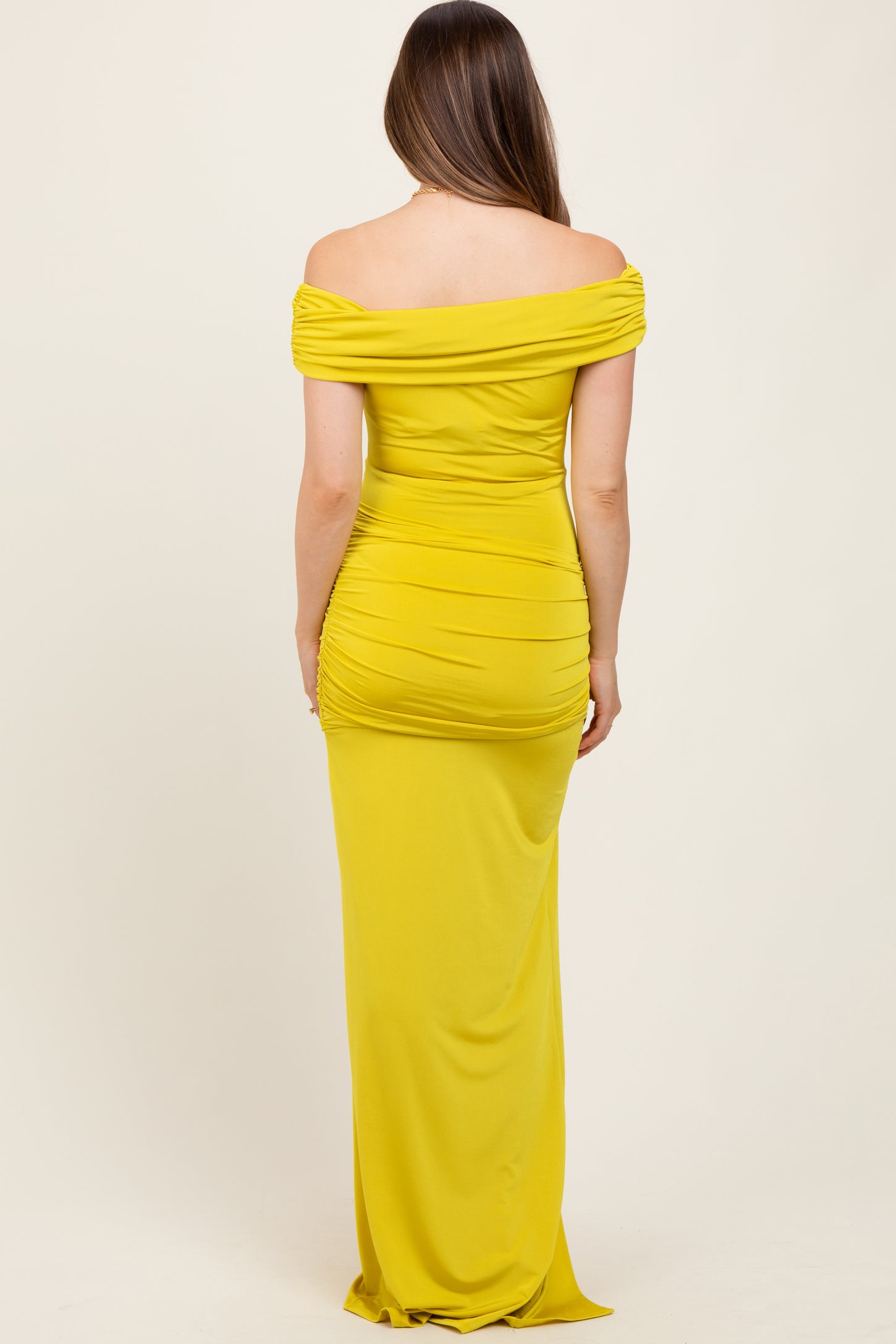 woman wearing a bright yellow off-the-shoulder maternity gown with ruching and a floor-length design