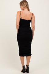 woman wearing a black ruched midi dress with thin straps and a fitted silhouette