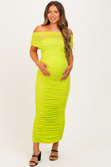 woman wearing a bright lime green off-shoulder maternity dress with ruching and holding her baby bump