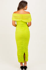 woman wearing a bright green off-the-shoulder maternity dress with ruching details and a back slit