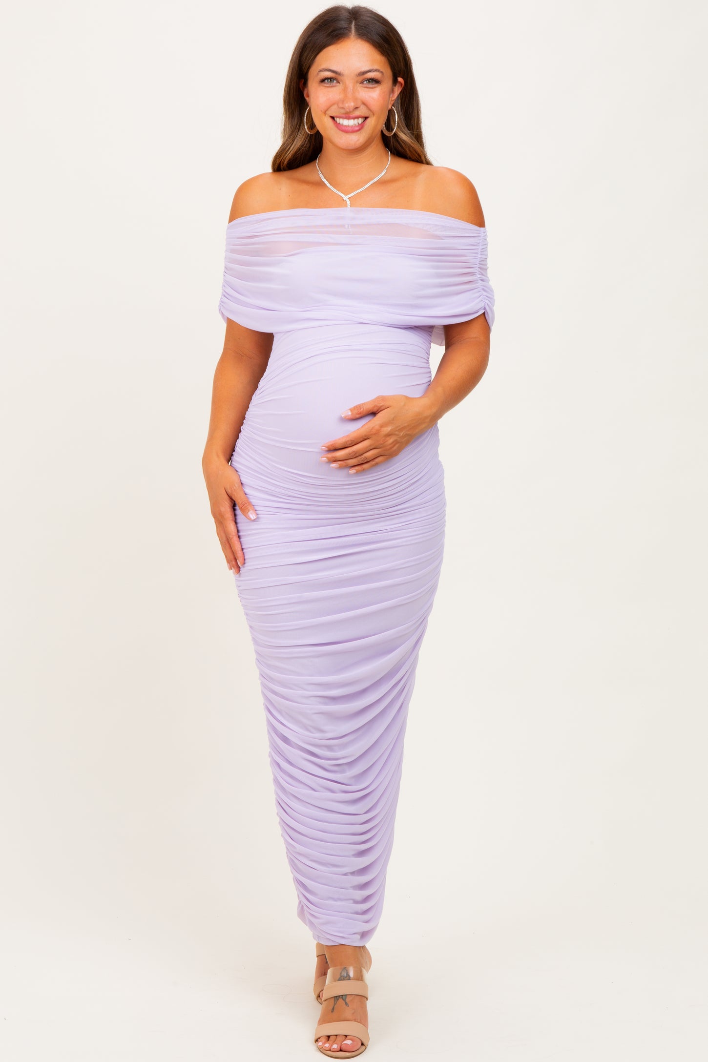 woman wearing a lavender off-the-shoulder maternity dress with ruched details and holding her baby bump