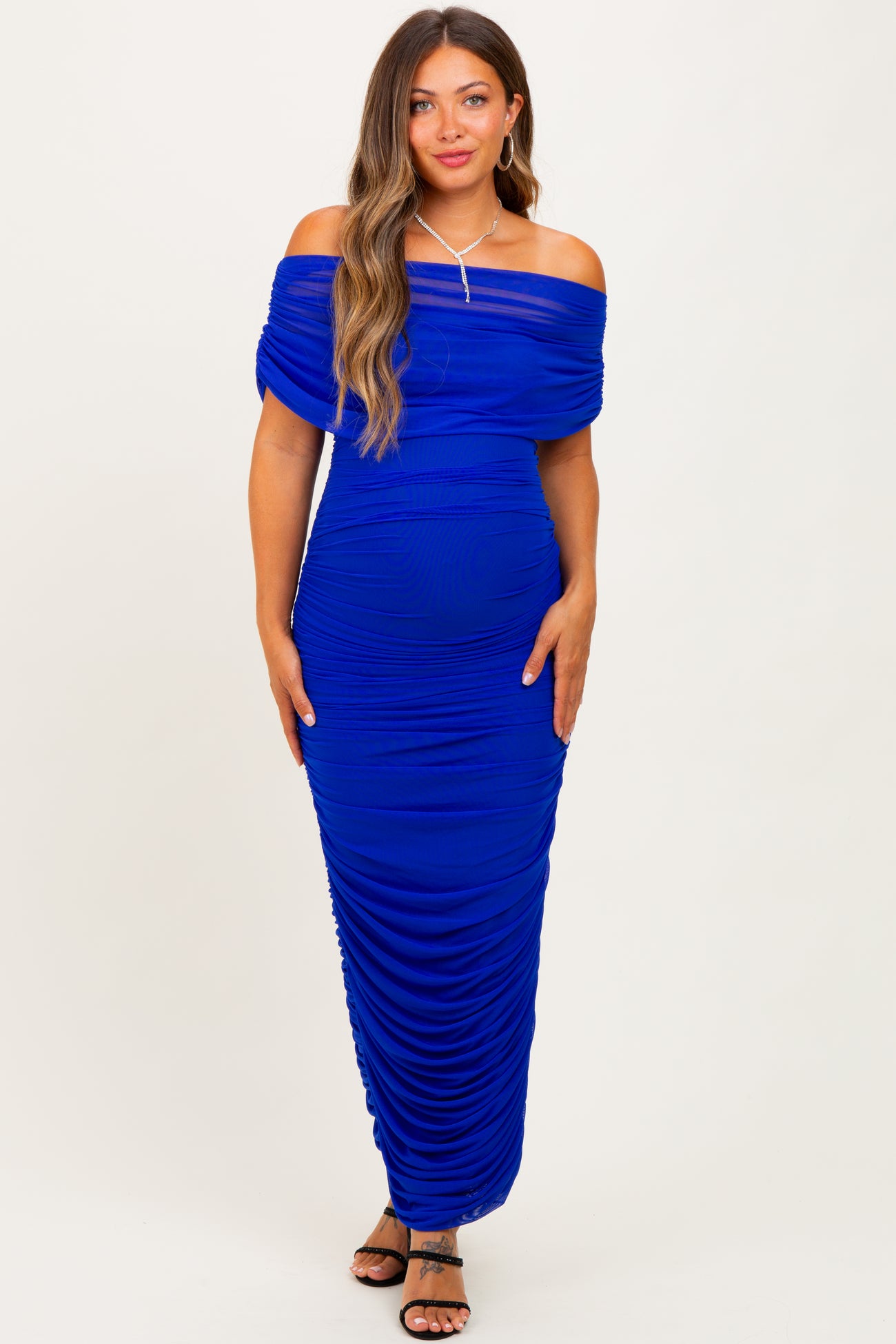 woman wearing a royal blue off-the-shoulder maternity dress with ruching and a visible baby bump