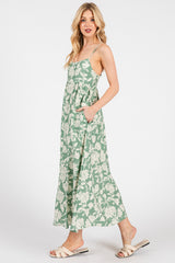 woman wearing a green floral maxi dress with adjustable straps and pockets, styled with beige slide sandals