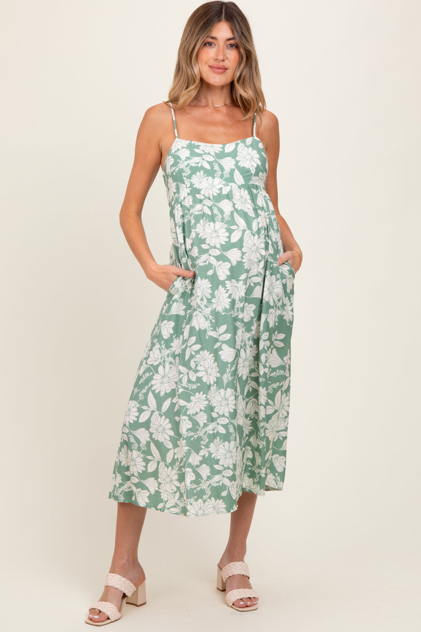woman wearing a green floral maternity dress with pockets and a baby bump visible