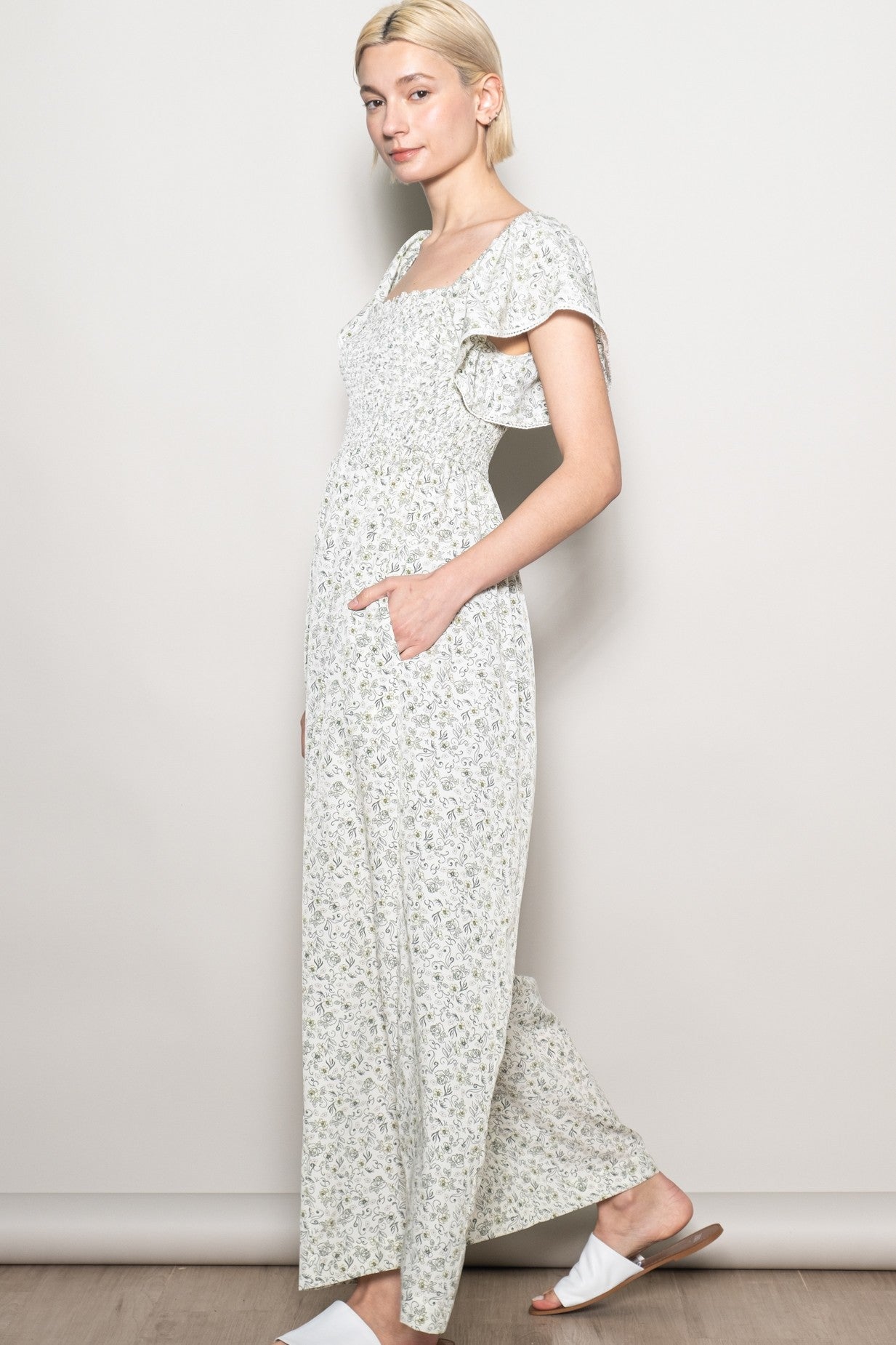 woman wearing a light green floral maxi dress with short flutter sleeves and side pockets
